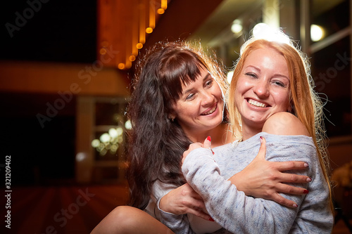 Two female friends having fun on a city street at night. Girls near illuminated building and black background with light in evening time