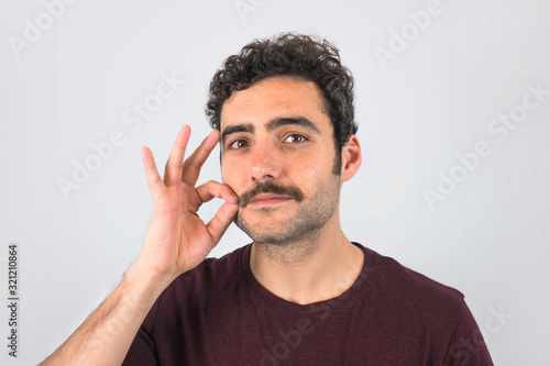 Brown, smiling, handsome man touching his mustache with purple t-shirt. Funny portrait. Gray background. photo