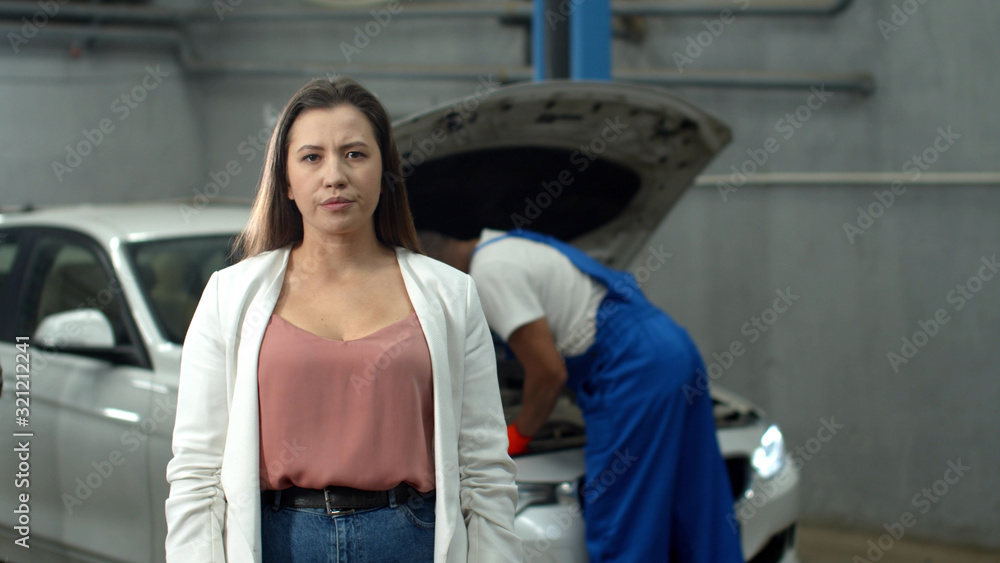 Mechanic repairs a car, dissatisfied woman looks at the camera Mechanic repairs a car, dissatisfied woman looks at the camera