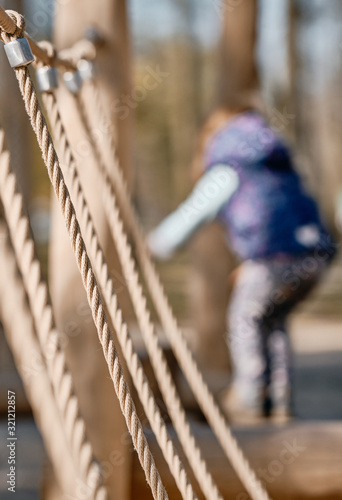 Close-up of some outdoor play equipment with ropes on a sunny springtime day with a child in the background. Seen in Germany in April. April 2019