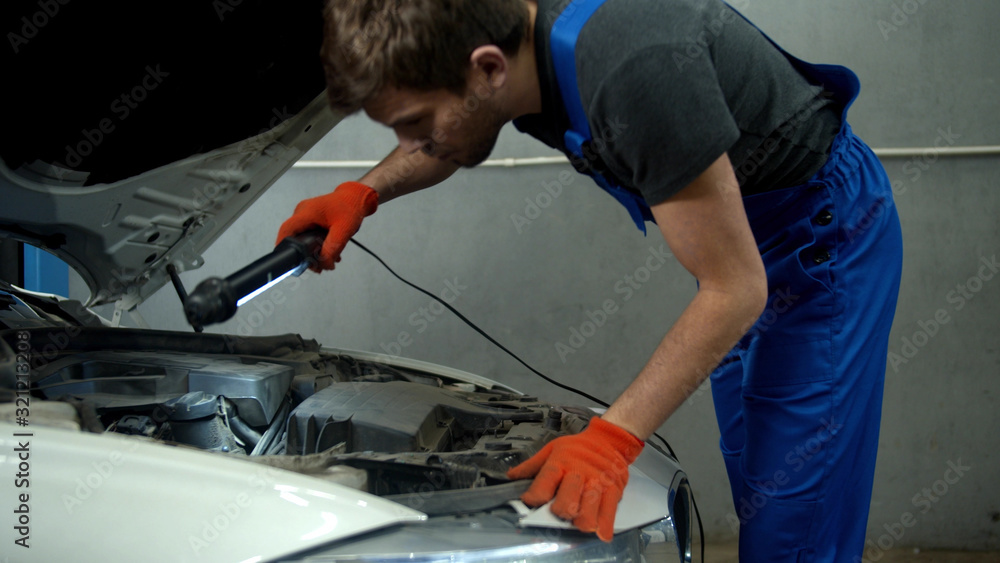 Slow motion, mechanic opens the hood of a car and turns on a flashlight Slow motion, mechanic opens the hood of a car and turns on a flashlight