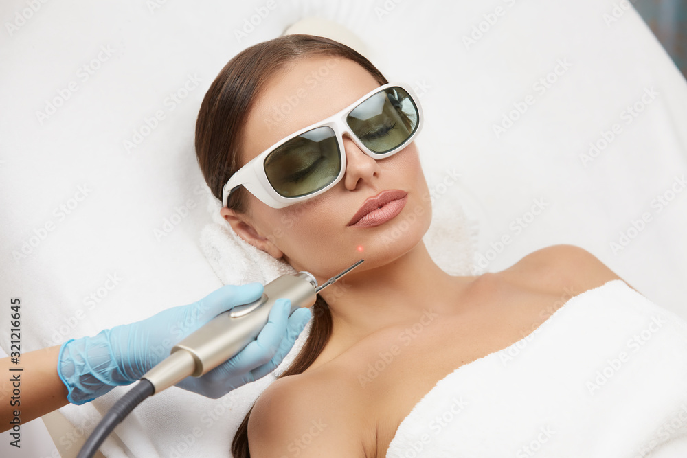Naklejka premium close-up of petty woman receiving laser procedures for her chin wearing protection glasses