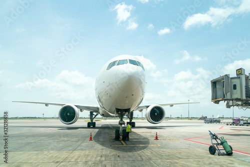 technician or engineer safety check of modern passenger or cargo airplane parking at terminal gate of international airport on a cloudy blue sky background