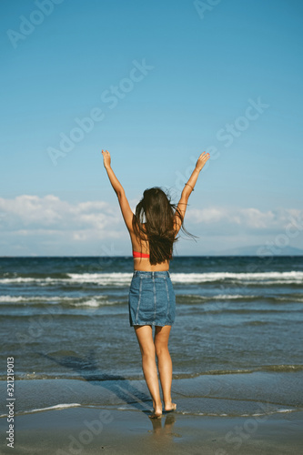 Happy woman standing on the beach with hands up.