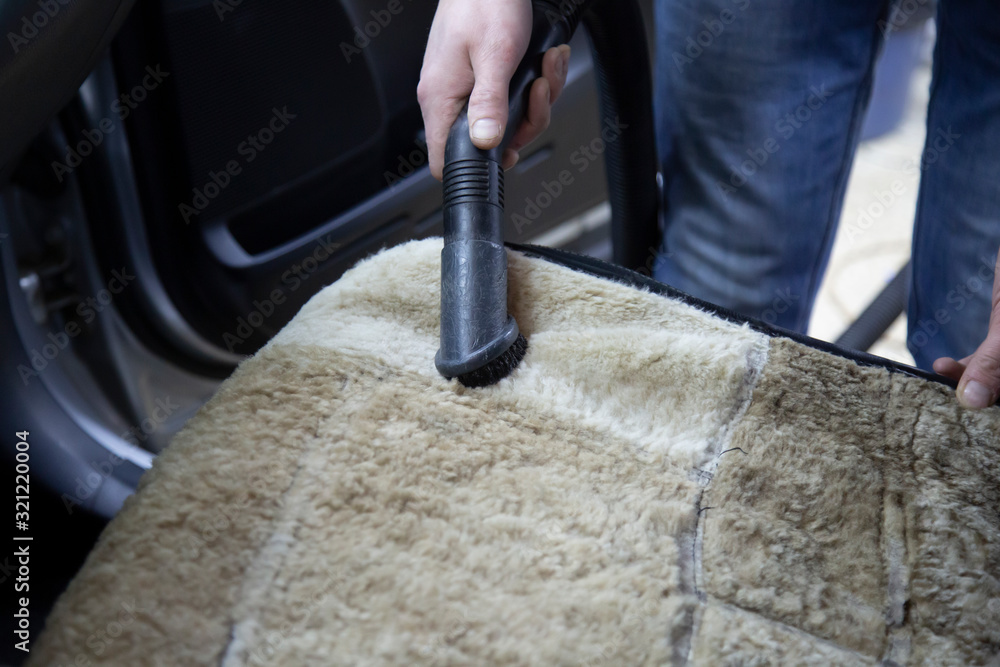 A man uses a vacuum cleaner to clean the car.