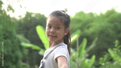 slow motion shot. A happy little girl in a white t-shirt with a long haircut is smiling at the camera on the nature outdoors.