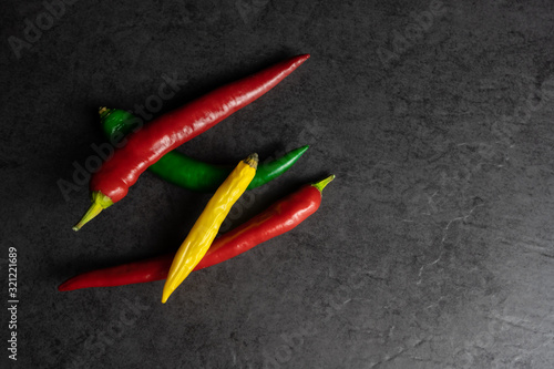 A group of fresh red, green, and yellow chili pepper on black background, copy space and top view
