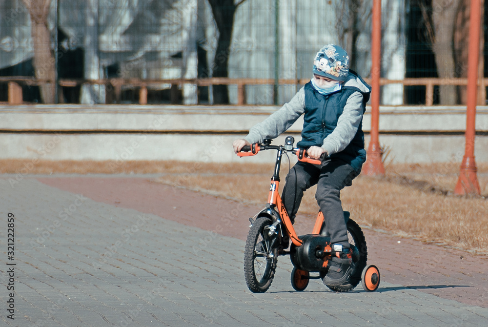 Child with medical mask. The child rides a bicycle in the park. Central Park, USA, New York. February, 01, 2020