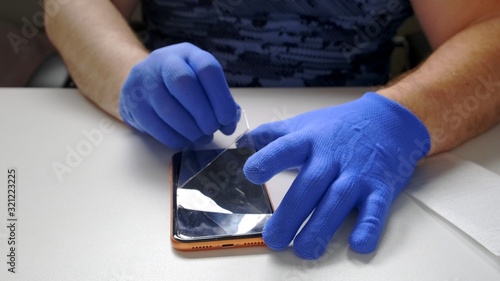 male hand in blue gloves replaces a broken tempered glass screen protector for a smartphone. A man prepares a smartphone to replace glass. Smartphone repair concept