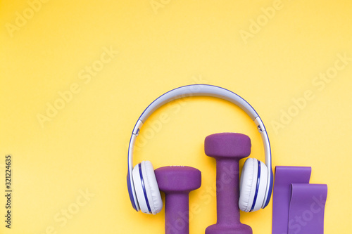 violet rubber expanders, purple dumbbells and headphones worn on them on a yellow background, copy space, top view, equipment for training at home and in the gym, healthy lifestyle concept photo