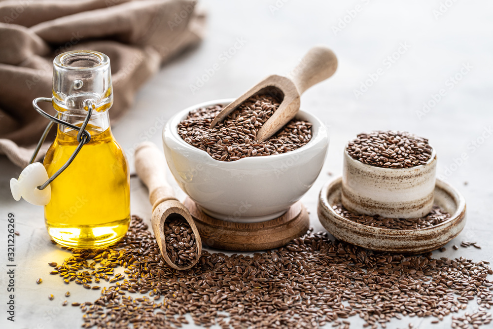 Flaxseed oil in a bottle and ceramic bowl with brown flax seeds and wooden spoon on a white background Flaxseed oil in a bottle and ceramic bowl with brown flax seeds and wooden spoon on a white background