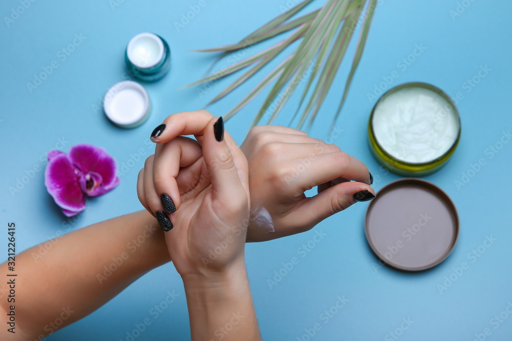 woman's hands apply cream each other on blue background with cosmetic products jars woman's hands apply cream each other on blue background with cosmetic products jars