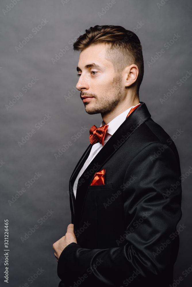 Fashion portrait of handsome elegant man with curly hair wearing tuxedo posing on gray background in studio Fashion portrait of handsome elegant man with curly hair wearing tuxedo posing on gray background in studio