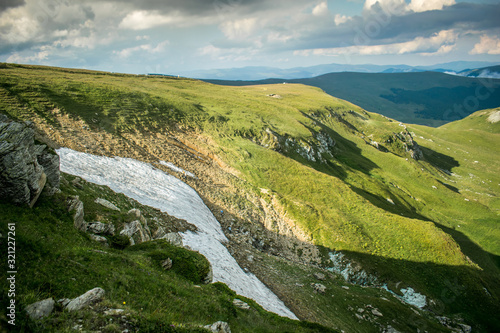 a beautiful mountain scenery. The heights of the mountains covered with grass and snow in July. A dramatic sky