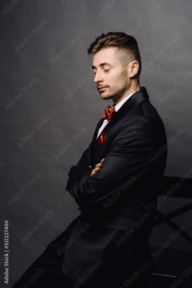 serious business man in elegant double breasted suit sitting on a chair on grey studio background serious business man in elegant double breasted suit sitting on a chair on grey studio background