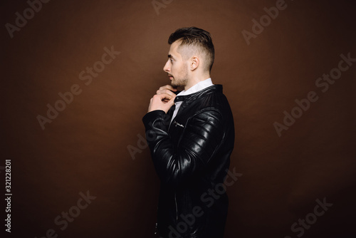 Handsome young man isolated. Fashionable man in leather jacket is standing on brown background.