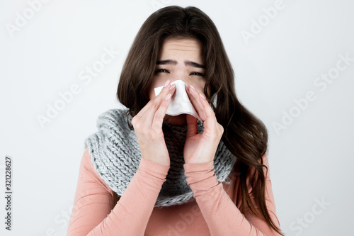 young beautiful brunette woman in knited scarf standing on isolated white background is about to sneeze, suffer from flu or virus, healthcare concept