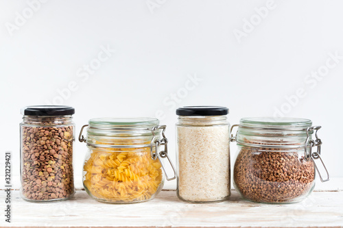 A variety of crops (buckwheat, rice, pasta, chickpeas) in glass jars on a wooden table on a light background. Close-up. The concept of vegetarianism and a balanced diet.