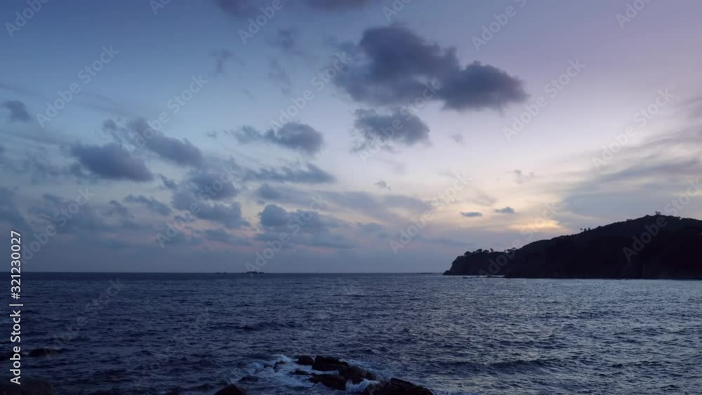 Dark island surrounded foamy waves under cloudy sky Dark island surrounded foamy waves under cloudy sky