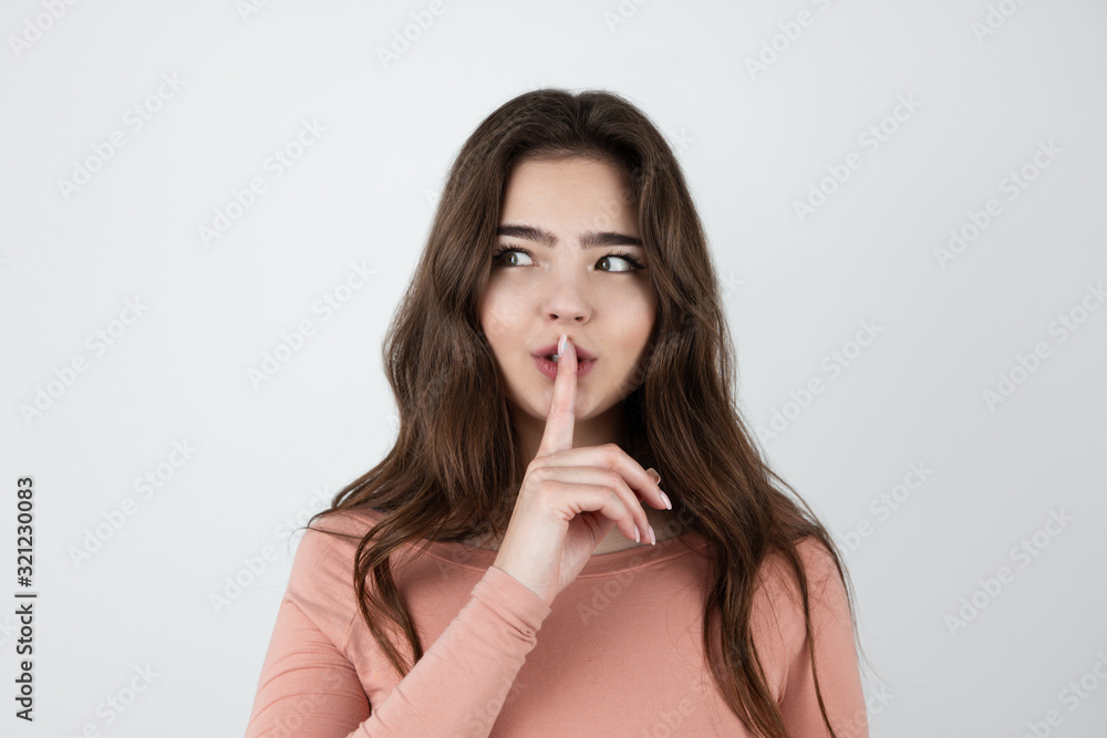 young beautiful brunette woman holding her finger near her lips showing silence sign standing on isolated white background young beautiful brunette woman holding her finger near her lips showing silence sign standing on isolated white background