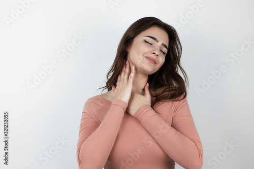 young beautiful woman touches her neck with both hands standing on isolated white background looking satisfied , pure beauty