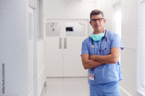 Portrait Of Mature Male Doctor Wearing Scrubs Standing In Hospital Corridor photo