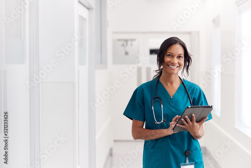 Portrait Of Smiling Female Doctor Wearing Scrubs In Hospital Corridor Holding Digital Tablet photo
