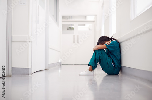 Billede på lærred Stressed And Overworked Female Doctor Wearing Scrubs Sitting On Floor In Hospita