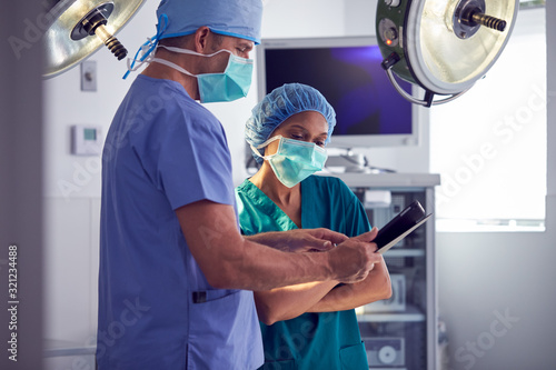 Male And Female Surgeons Wearing Scrubs Looking At Digital Tablet In Hospital Operating Theater photo