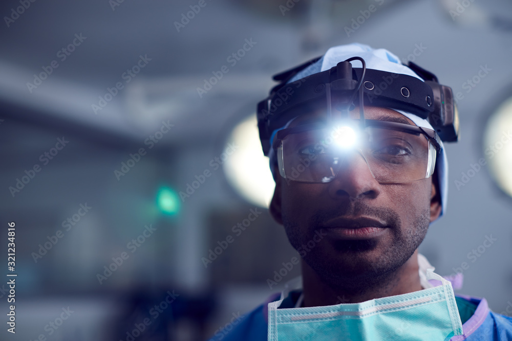 Portrait Of Male Surgeon Wearing Protective Glasses And Head Light In Hospital Operating Theater Portrait Of Male Surgeon Wearing Protective Glasses And Head Light In Hospital Operating Theater