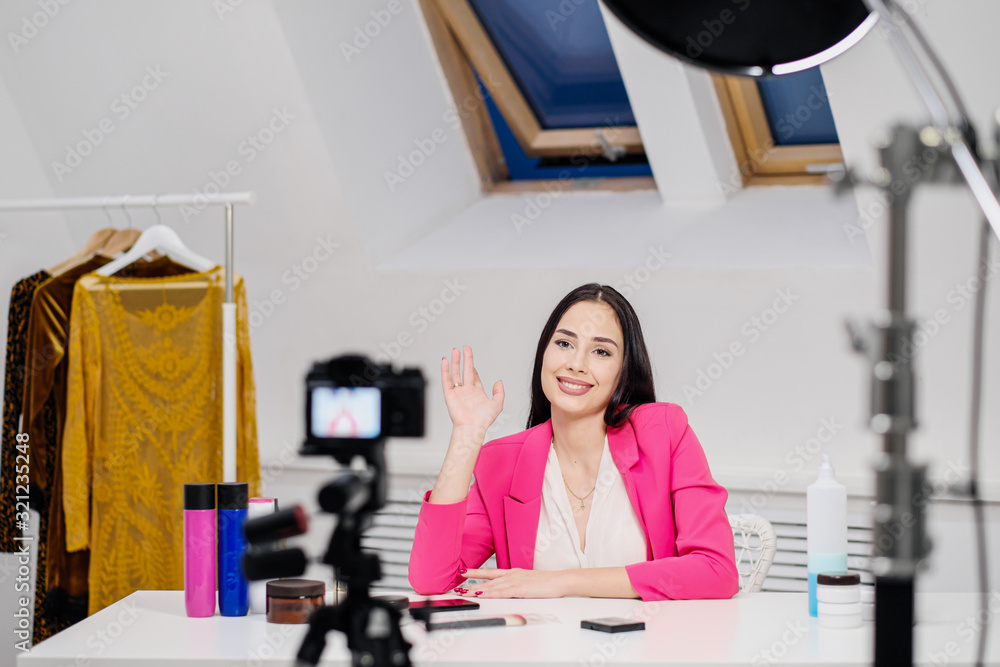 A female beauty blogger records a video in a white room. Lighting and camera on a tripod.