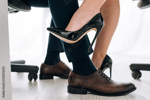 cropped view of secretary in heels touching leg of businessman in office