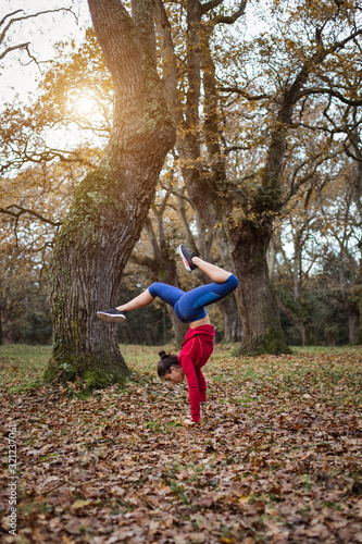 Young woman doing handstand outdoor in autumn. Female fit athlete doing gymnastic balance exercise in nature.