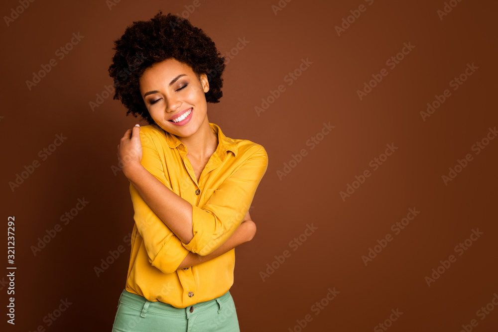 Photo of charming beautiful dark skin lady holding shoulders eyes closed enjoy love herself nice blouse clothes wear yellow shirt green trousers isolated brown color background Photo of charming beautiful dark skin lady holding shoulders eyes closed enjoy love herself nice blouse clothes wear yellow shirt green trousers isolated brown color background