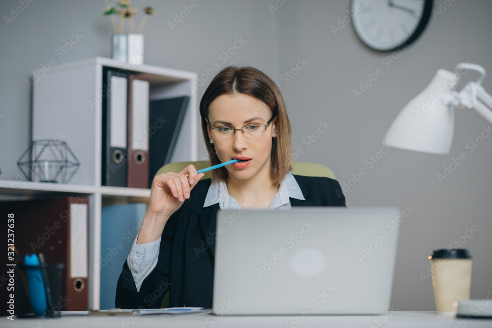 Attractive woman in eye glasses enjoying her favourite freelance job working in home on laptop computer. Female freelancer using netbook and writing ideas in notepad Attractive woman in eye glasses enjoying her favourite freelance job working in home on laptop computer. Female freelancer using netbook and writing ideas in notepad
