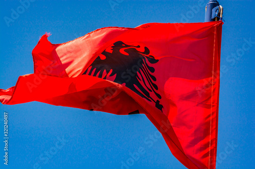 Fotografie Red albanian flag flying in the wind on blue sky