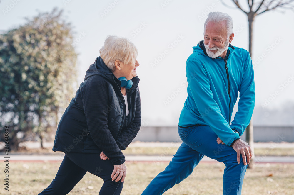 Obraz premium A senior adult male teaching a senior woman how to stretch in the park.