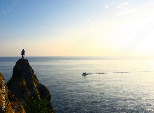 The men on the top of the cliff above the sea. The boat speeding on the sea surface