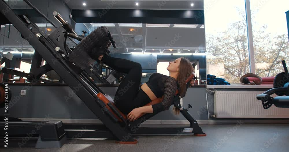 Female athlete in the gym. Side view attractive girl with long red hair in black sporty clothes performing exercises for legs muscles on simulator. 4K 50 FPS slow motion. Female athlete in the gym. Side view attractive girl with long red hair in black sporty clothes performing exercises for legs muscles on simulator. 4K 50 FPS slow motion.