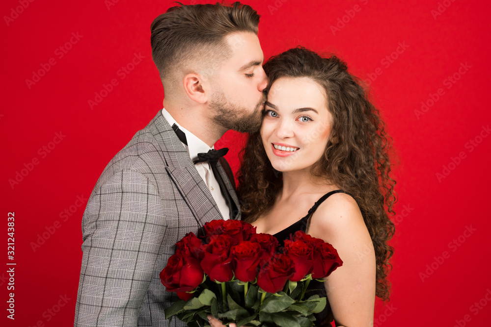 Young man kissing smiling girlfriend isolated on red background Young man kissing smiling girlfriend isolated on red background