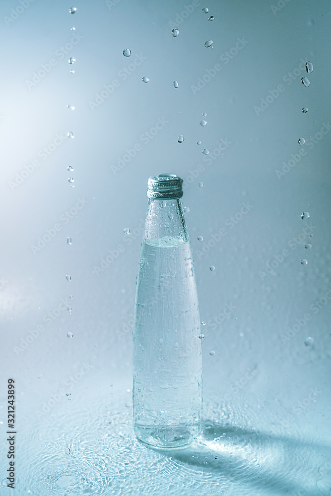 Glass bottle and water splashes and falls on white blue background. Freshness and life-giving power of water. Thirst Glass bottle and water splashes and falls on white blue background. Freshness and life-giving power of water. Thirst