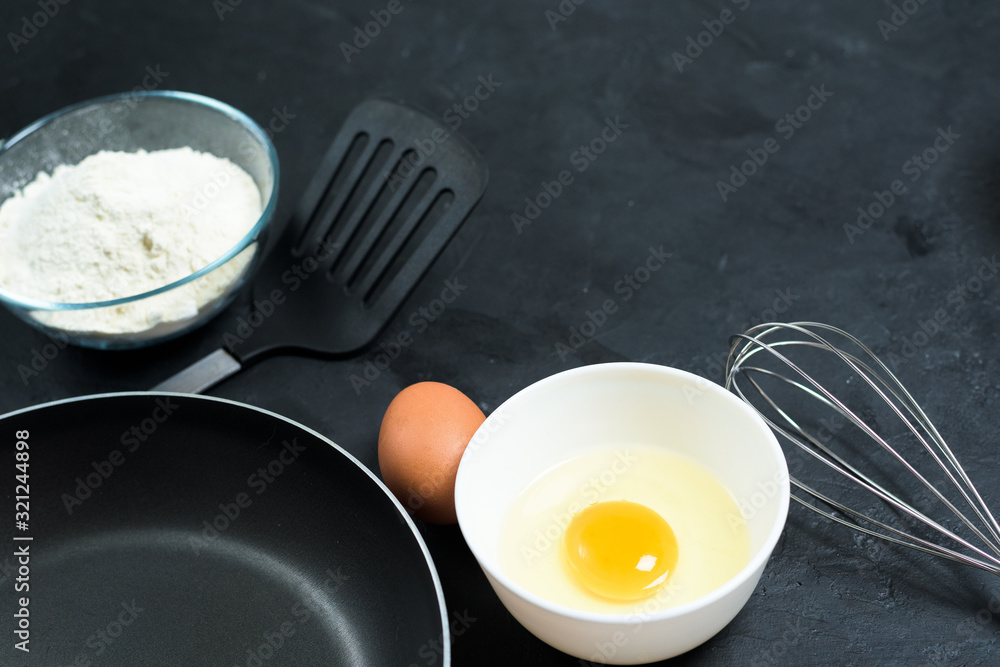 Maslenitsa.Ingredients for baking pancakes. frying pan, eggs, flour, egg beater, on a black background top view. top view, place to copy text, recipe. Maslenitsa.Ingredients for baking pancakes. frying pan, eggs, flour, egg beater, on a black background top view. top view, place to copy text, recipe.