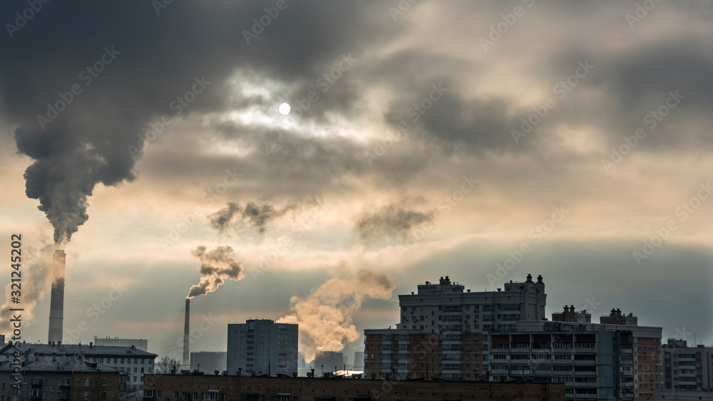 The dark silhouette of the city against the background of a cloudy dramatic sky, through which the setting sun shines