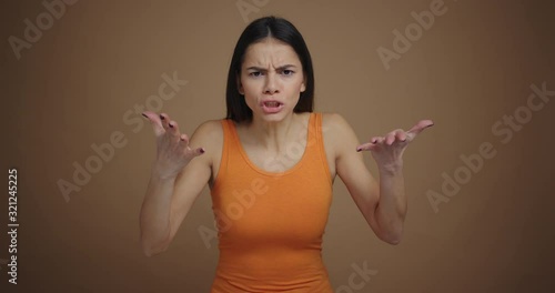 Angry young woman swears and gesturing with hands looking at the camera on brown background isolated photo