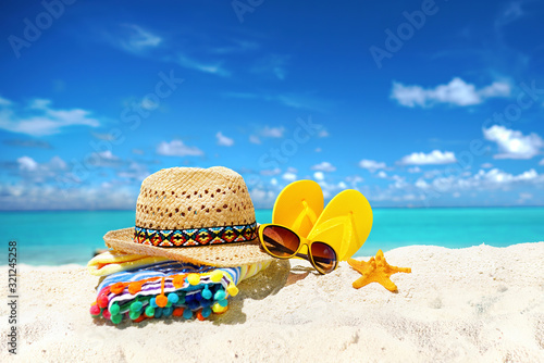 Concept summer beach holiday. Beach accessories - straw hat, glasses, towel, starfish, yellow flip-flops on a sandy beach against blue sky with clouds and bright sun. Beautiful colorful image.