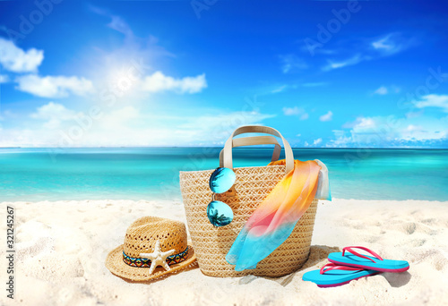 Concept summer holiday. Accessories - bag  straw hat  sunglasses with palm tree reflection  pareo  flip-flops on sandy beach against ocean  blue sky  clouds and bright sun. Beautiful colorful image.