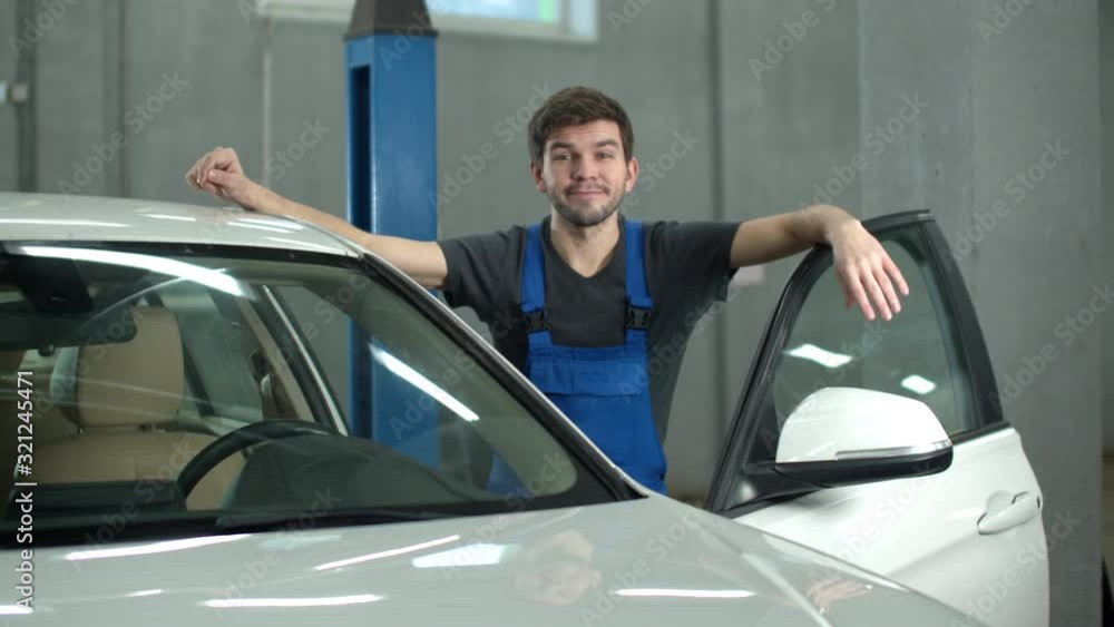 Slow motion, mechanic is standing near a car and smiling Slow motion, mechanic is standing near a car and smiling