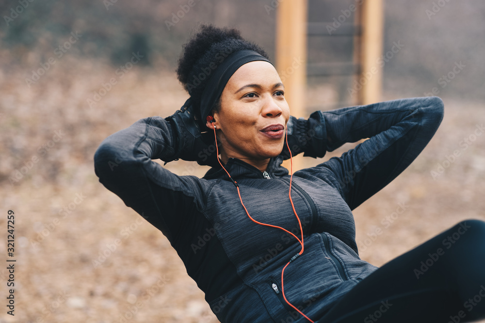 Naklejka premium A young woman doing situps outdoors while listening to the music.