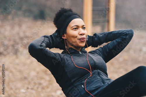 A young woman doing situps outdoors while listening to the music.