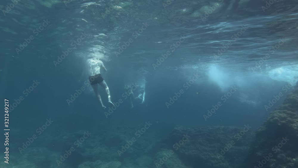 Tree tourists man and womans floats on the surface of water in sunbeams. Underwater shot. Mediterranean Sea, Greece Tree tourists man and womans floats on the surface of water in sunbeams. Underwater shot. Mediterranean Sea, Greece